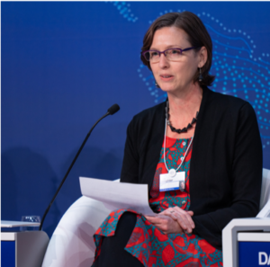A woman with short brown hair and glasses speaks in front of a microphone at the World Economic Forum.
